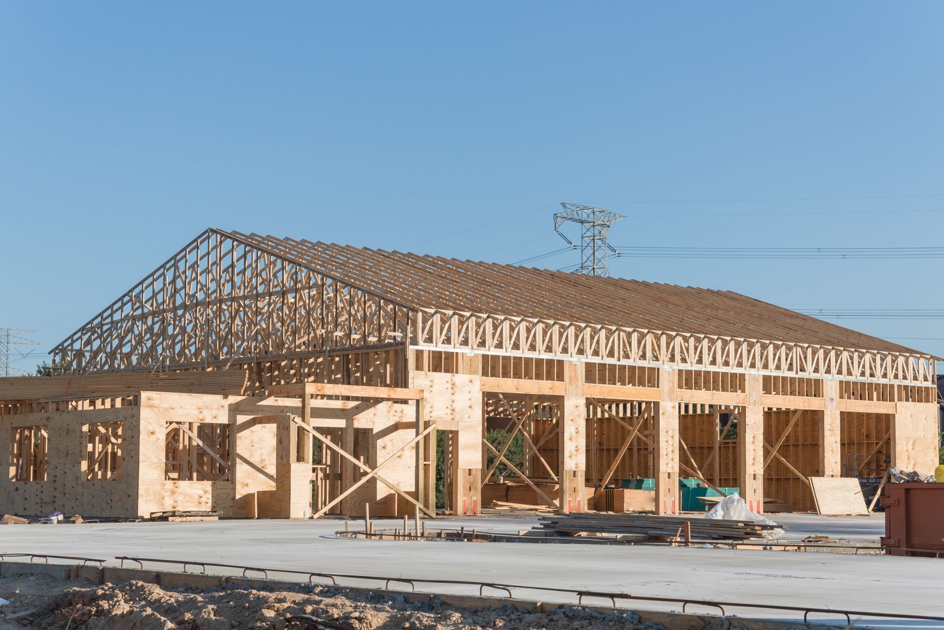 Wood frame house under construction with foundation in Humble, Texas, USA. New stick built framing one floor commercial building clear blue sky. Pile of beams, log, sand, gravel. Industrial background